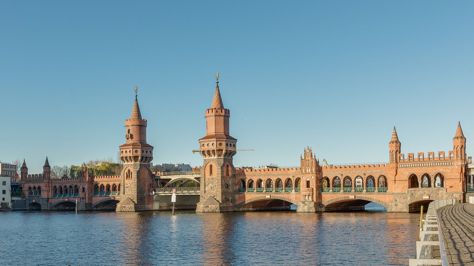Backsteinbau der Oberbaumbrücke mit zwei Türmen und Bogengängen über der Spree im warmen Abendlicht