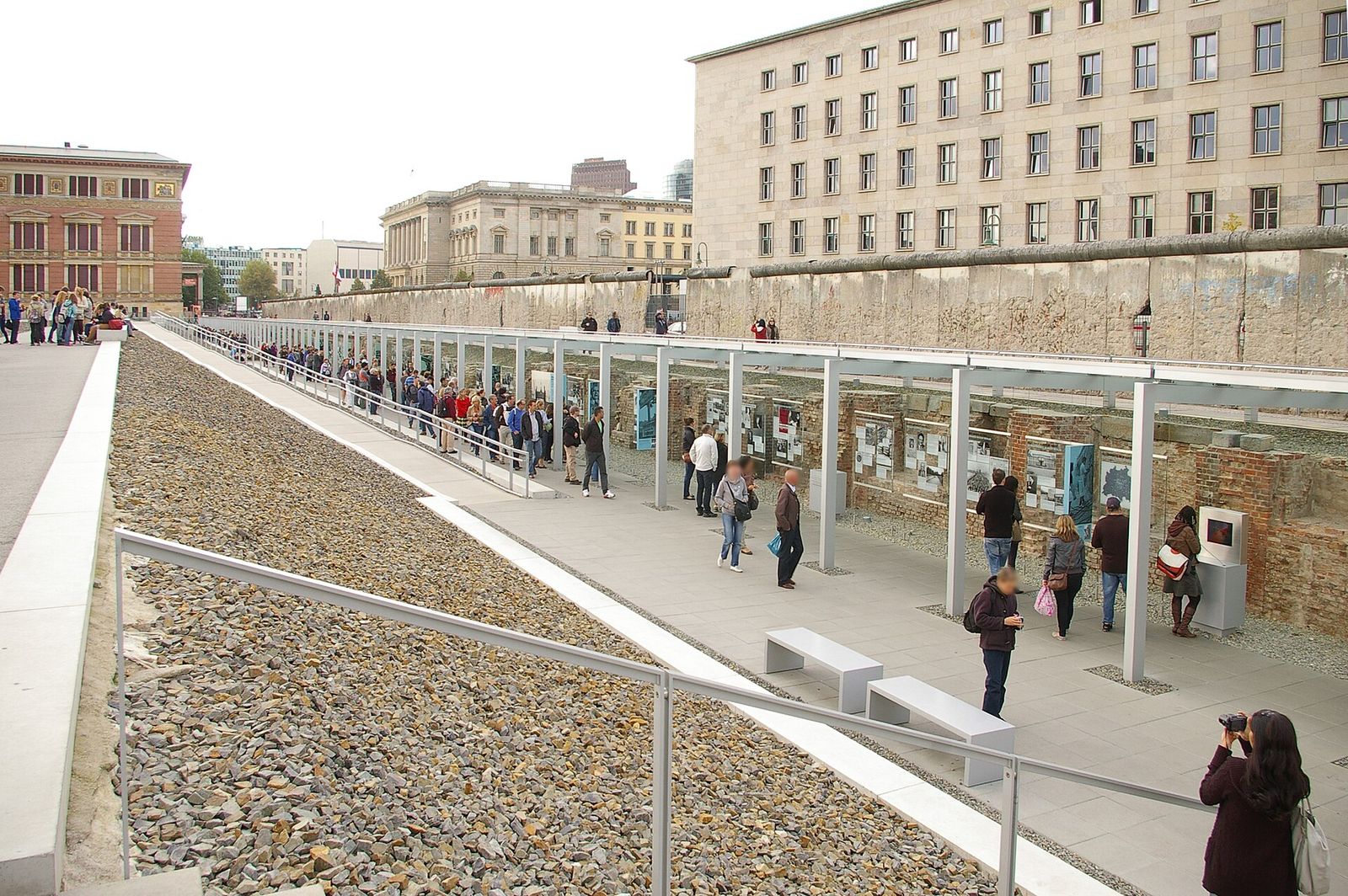 Mauerabschnitt an der Niederkirchnerstraße oberhalb des Ausstellungsgrabens der Topographie des Terrors; im Vordergrund Besucher vor Infotafeln