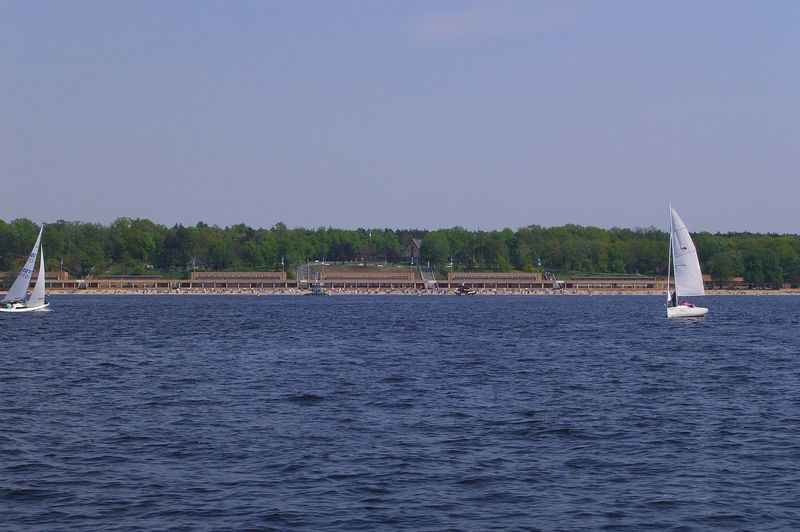 Segelboote auf dem Wannsee, im Hintergrund die langgestreckten Hallen des Strandbads Wannsee am bewaldeten Ufer