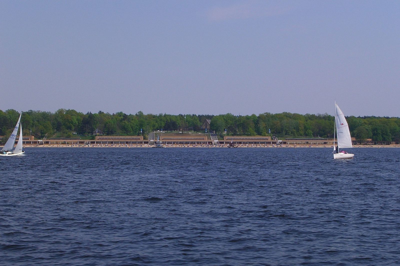 Segelboote auf dem Wannsee vor den langen Hallen des Strandbads Wannsee am bewaldeten Ufer